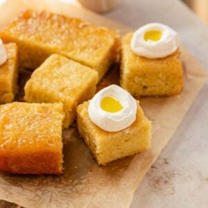 slices of upside down lemon olive oil cake on a piece of parchment paper with dollops of whipped cream and olive oil