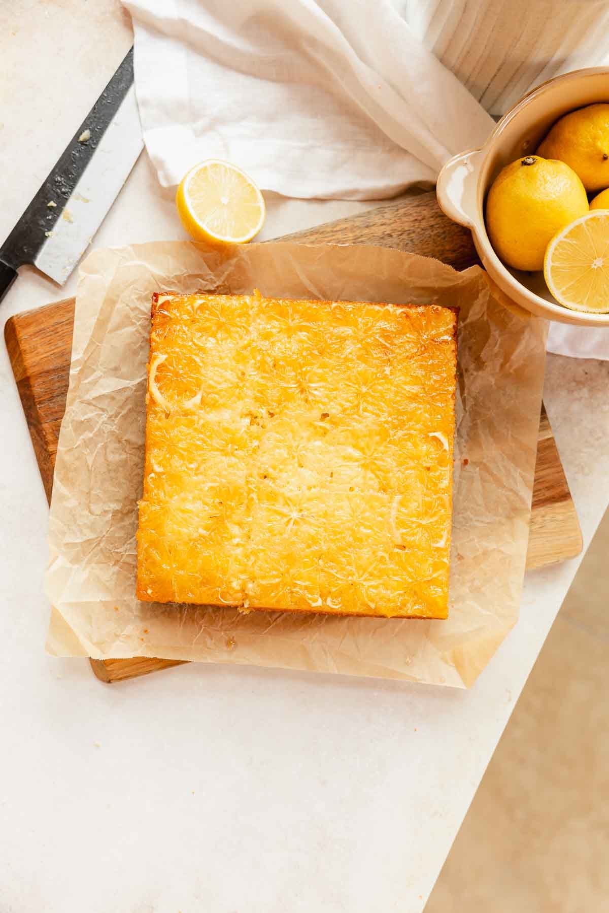 lemon olive oil cake upside down on a piece of parchment paper and cutting board