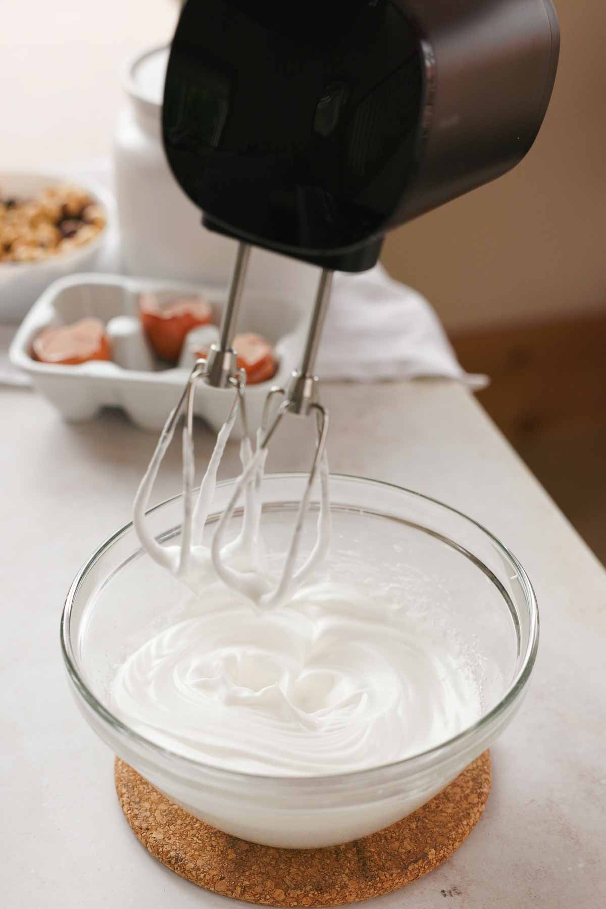 egg whites whipped to medium-stiff peaks in a glass bowl with electric handheld mixer
