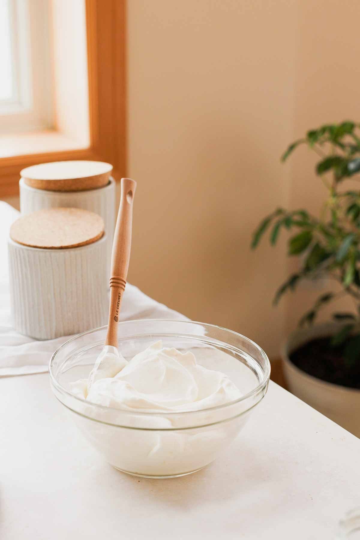 cream whipped to stiff peaks in a large glass bowl with a spatula