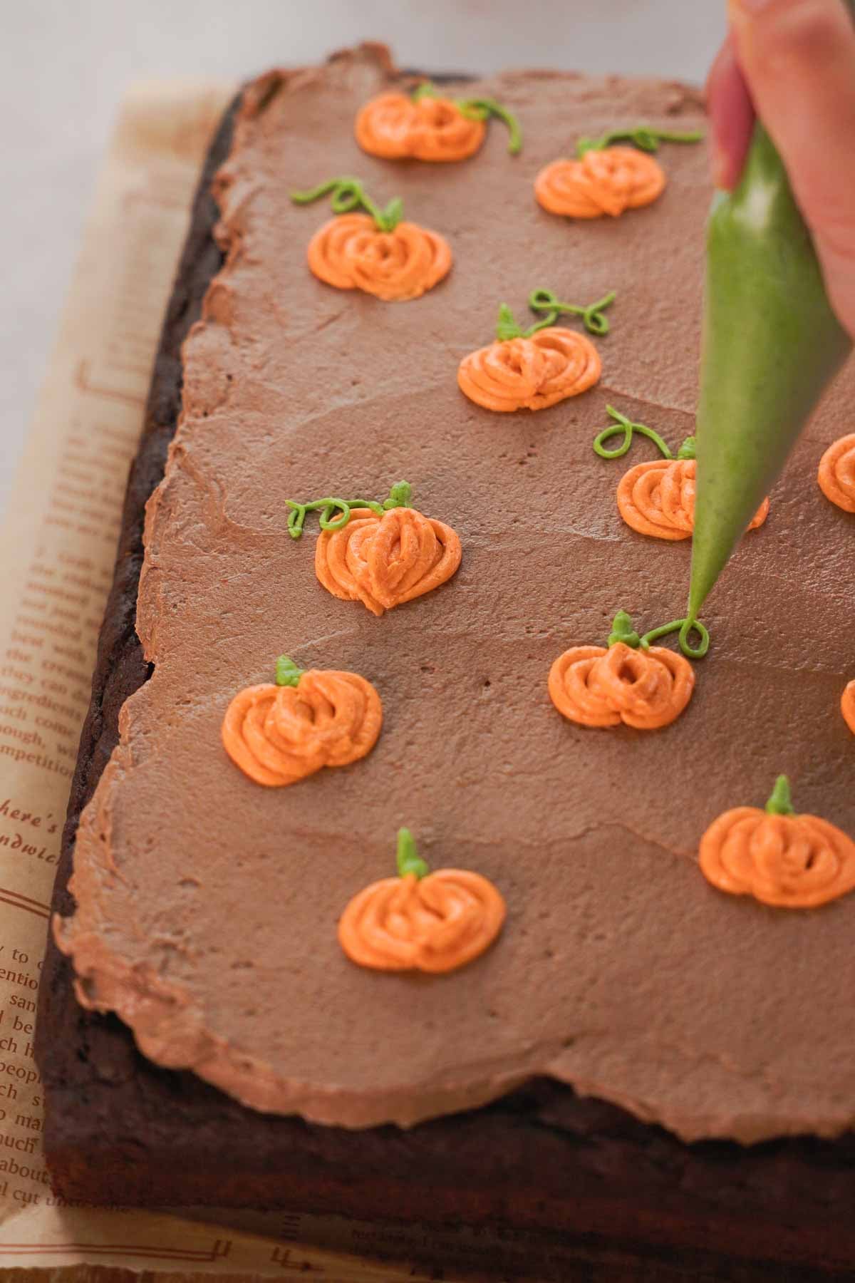 piping pumpkins onto chocolate frosted pumpkin cake