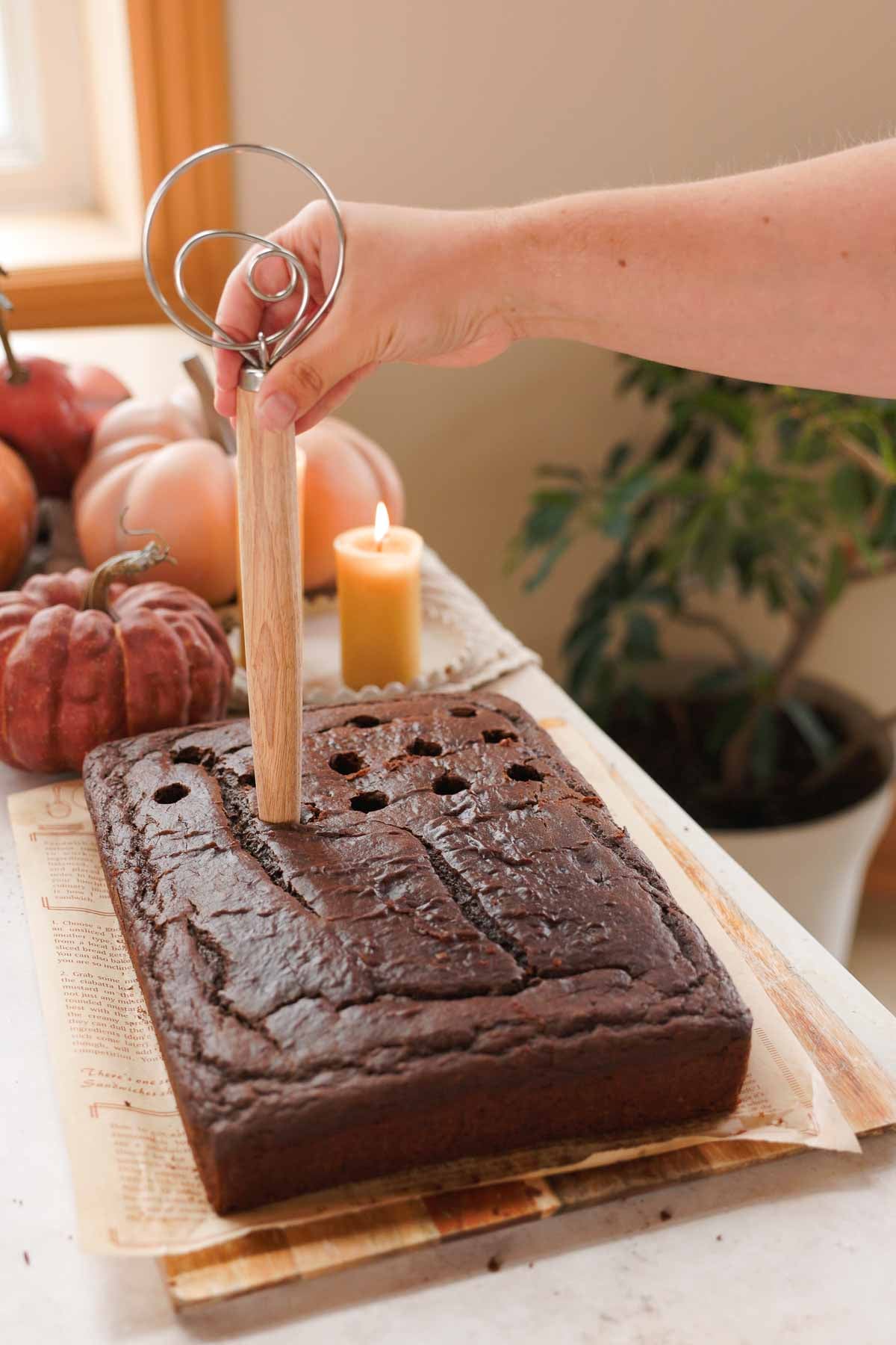 poking holes into chocolate pumpkin cake with the wooden handle of a whisk