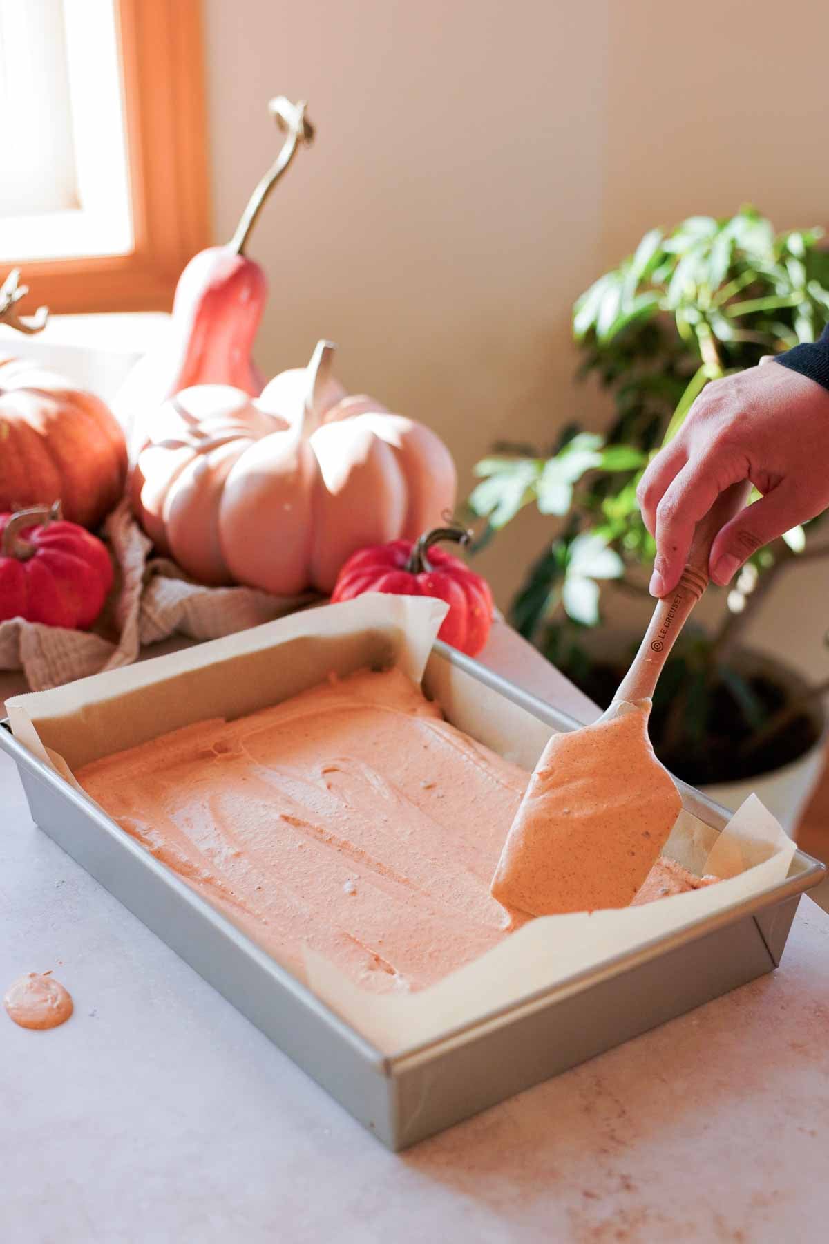 spreading pumpkin spice ice cream into parchment lined pan with spatula
